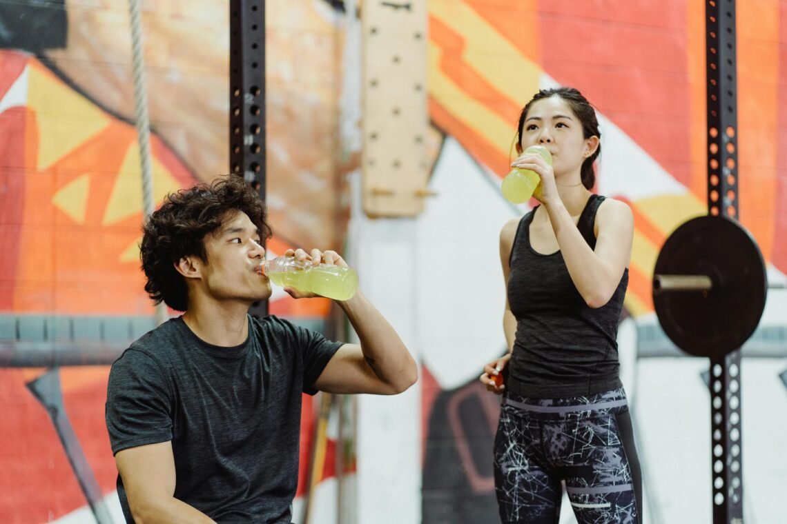 Photo of a Couple Drinking from Bottles in a Gym