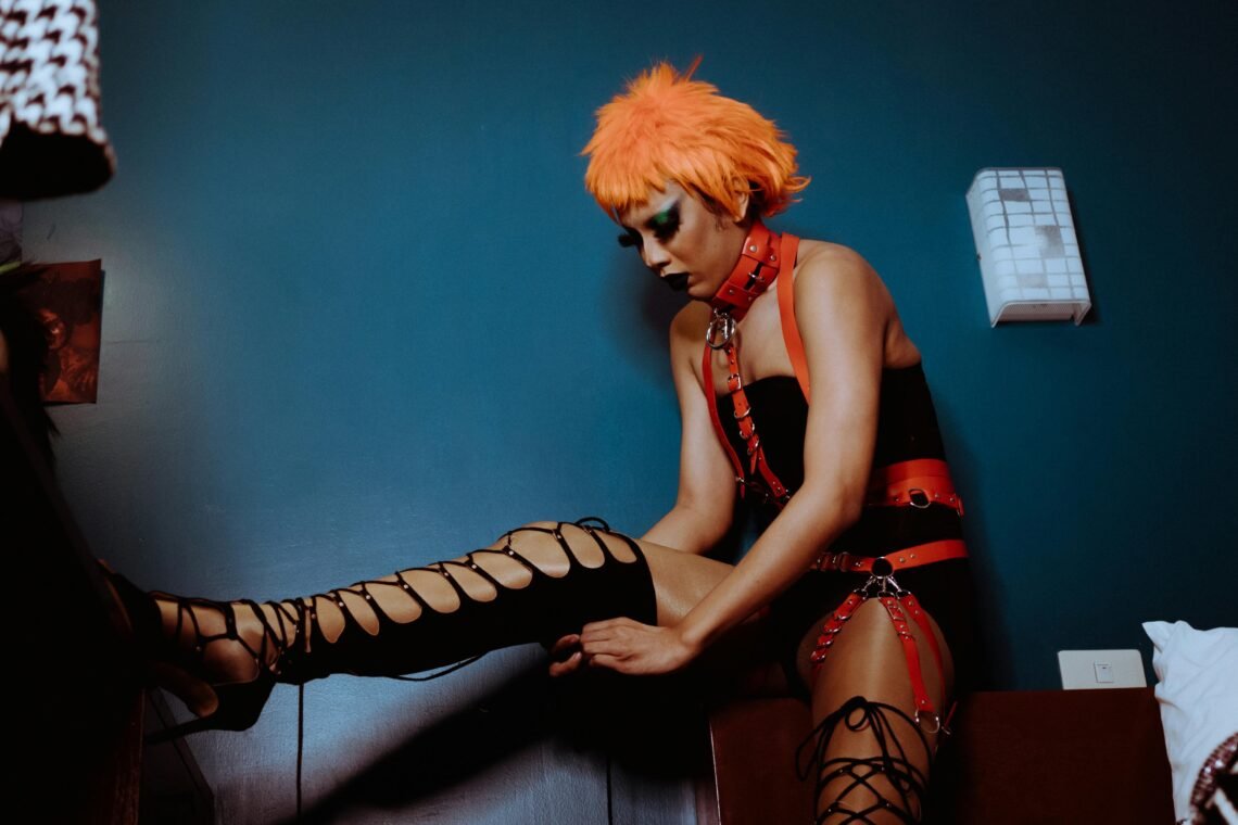 Bizarre woman in BDSM harness putting on thigh high shoes